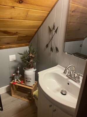 Ett badrum med ett träpanelat tak, en vit tvättställ och en dekorativ spegel.