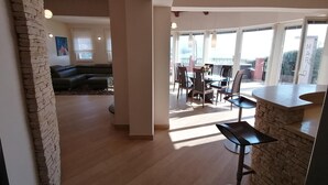 Amplia sala de estar con una pared de acento de piedra, un sofá de color oscuro y un comedor con mesa y sillas.