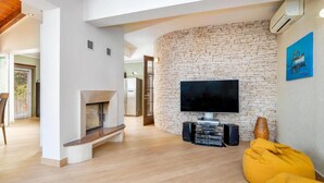 Una sala de estar moderna con pared de piedra, televisor de pantalla plana, chimenea y sillón orejero amarillo.