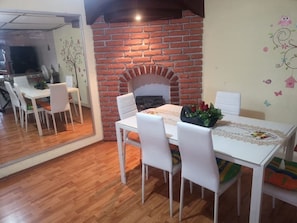A dining area with a brick fireplace, white chairs, and a table with a lace tablecloth.