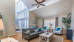 A spacious living room with a grey sofa, striped armchairs, a wooden coffee table, and a ceiling fan.