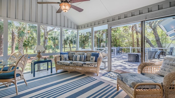 A sunroom with a large glass door, wicker furniture, and a ceiling fan.