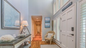 A hallway with a wooden floor, a wicker chair, a lamp, and a framed picture on the wall.