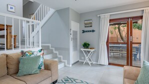 Uma sala de estar moderna com escada, área de jantar com assentos externos e vista para o exterior.