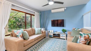 Sala de estar com sofá bege, tapete estampado e ventilador de teto.