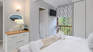 Quarto com cama, mesa de cabeceira com abajur, espelho, televisão e janela com vista para o verde.