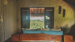 A wooden bed with floral bedding, a view of a lush landscape through an open doorway, and a bamboo curtain.