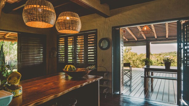 A wooden bar area with a bowl of fruit, wicker pendant lights, and a view of greenery outside.