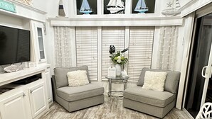 Een woonkamer met twee grijze banken, een glazen salontafel, een kroonluchter en een open haard met decoratieve zeilen.