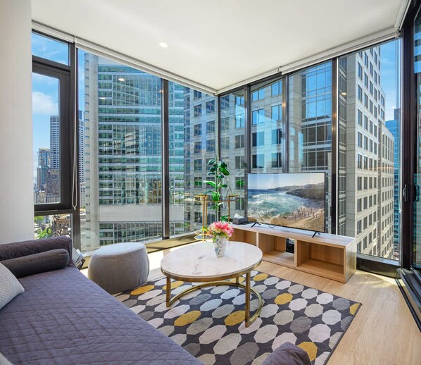 Relax in this stylish living room with a panoramic view of the city and beach, featuring a comfortable sofa, coffee table, and flat-screen TV.