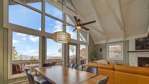 A spacious room with a large dining table, comfortable seating, a fireplace, and large windows offering a view of the outdoors. - Boho Chalet w/ Mountain Views (Beech Mountain)