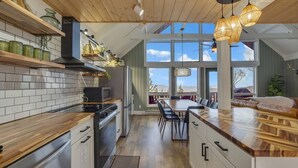 A modern kitchen with wooden cabinets, a central island, and a dining area with a view. - Boho Chalet w/ Mountain Views (Beech Mountain)
