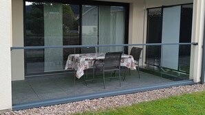 A modern building with a covered patio area featuring a table and chairs, a glass railing, and a view of the surrounding landscape. - Beautiful *** studio apartment with a terrace (Gérardmer)