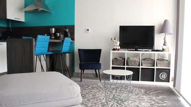 A modern living room with a sofa, a TV, a small table, and a kitchen area with chairs and a stove. - Beautiful *** studio apartment with a terrace (Gérardmer)