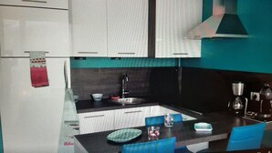 A modern kitchen with white cabinets, a black countertop, and a blue chair. - Beautiful *** studio apartment with a terrace (Gérardmer)