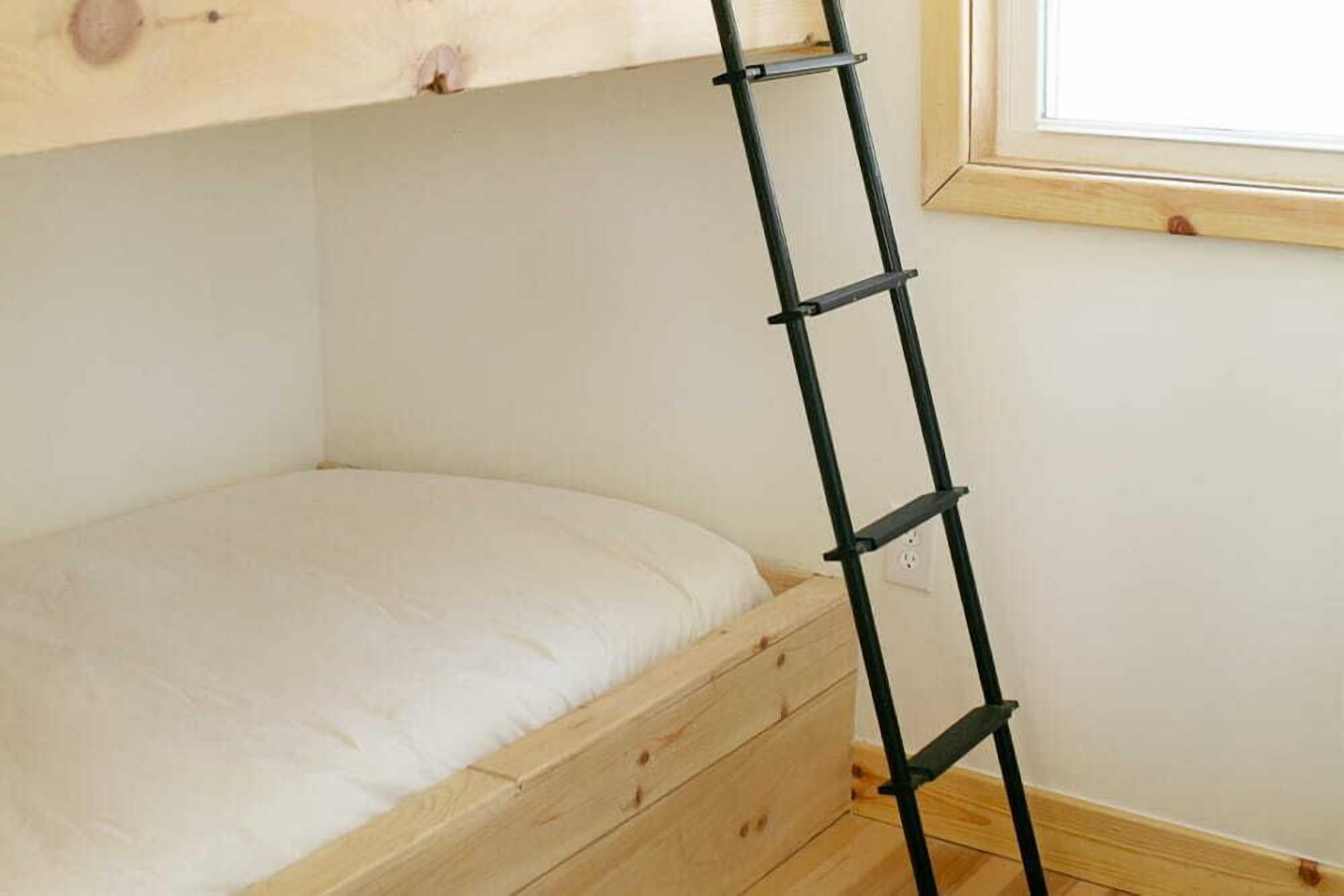 Een stapelbed met een ladder, houten lades en een raam.