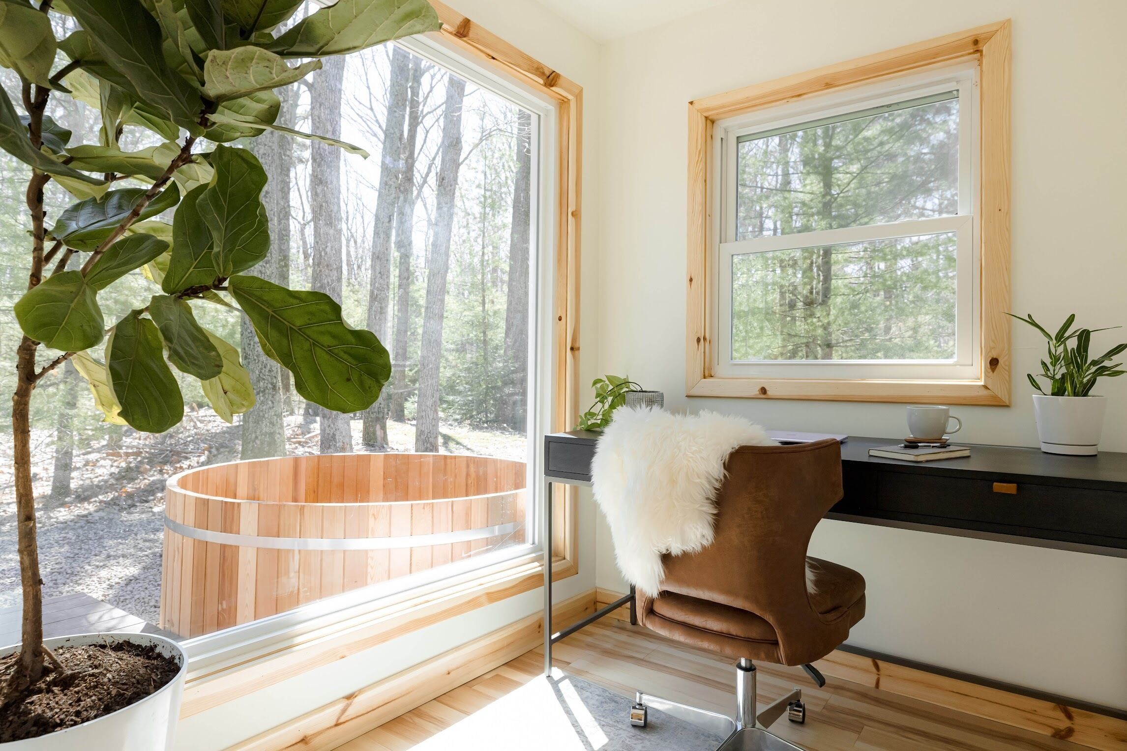 A room with a wooden hot tub, a brown chair, a window with a view of trees, and a potted plant on the windowsill.