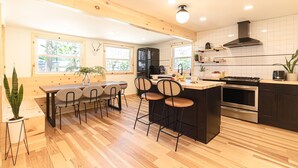 Una cocina moderna con suelo de madera, un comedor con mesa y sillas, y una isla grande con taburetes de bar.