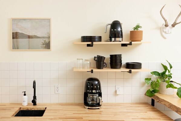 A kitchen with a coffee maker, shelves with dishes, a sink, and a mounted plant. - The Rex Hotel (Greentown)