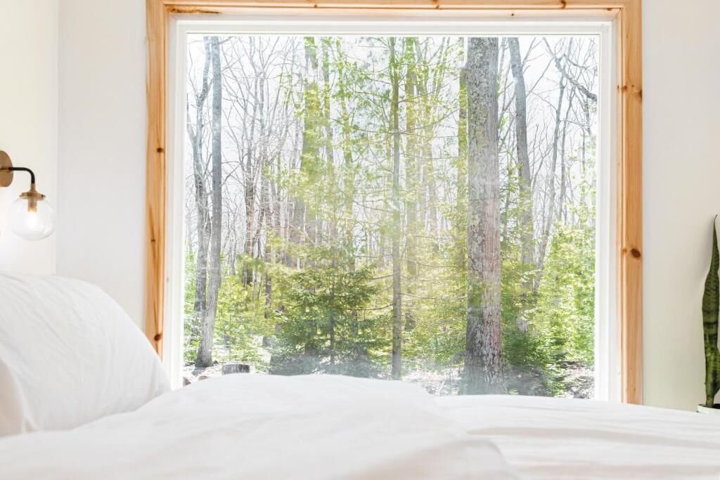 A bedroom with a large window offering a view of a forest.
