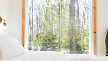 A bedroom with a large window offering a view of a forest.