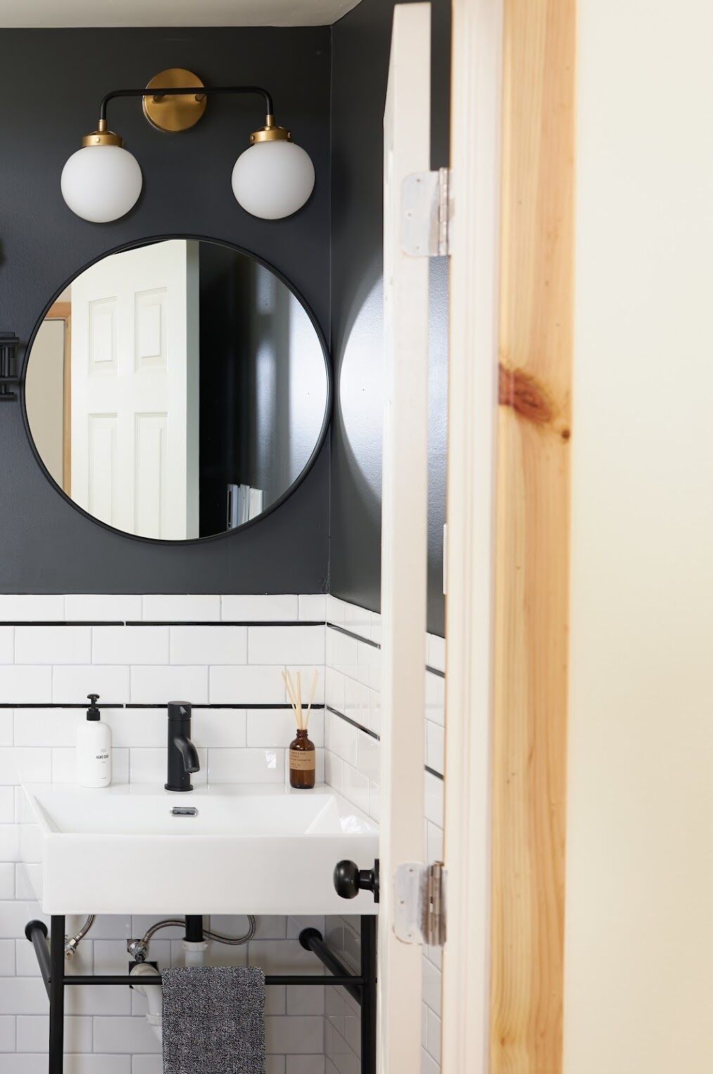 Une salle de bain avec un lavabo blanc, un robinet noir et un miroir rond au-dessus. Deux appliques murales en laiton sont fixées au mur.
