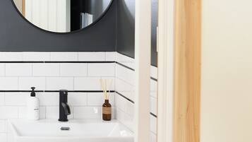 Une salle de bain avec un lavabo blanc, un robinet noir et un miroir rond au-dessus. Deux appliques murales en laiton sont fixées au mur.