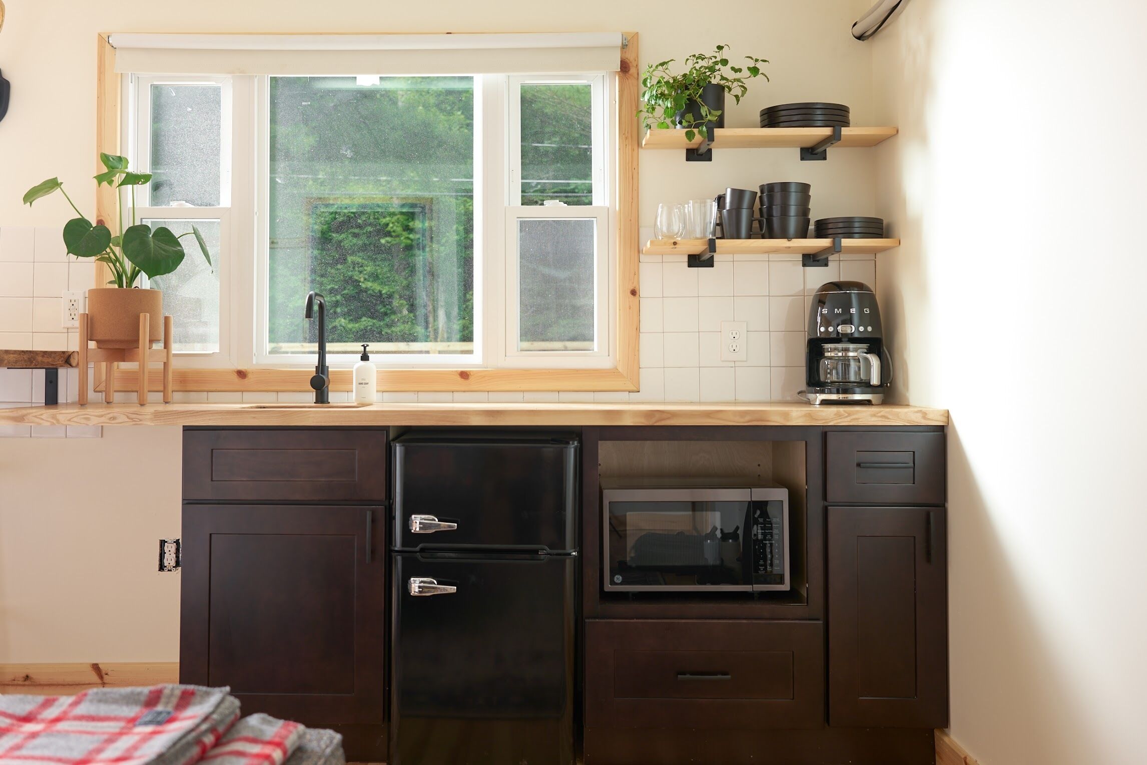 A compact kitchen with a window, a microwave, a coffee maker, and a potted plant.