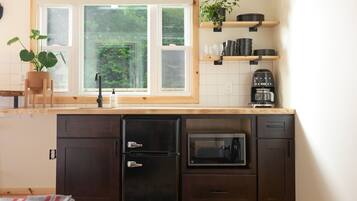 A compact kitchen with a window, a microwave, a coffee maker, and a potted plant.