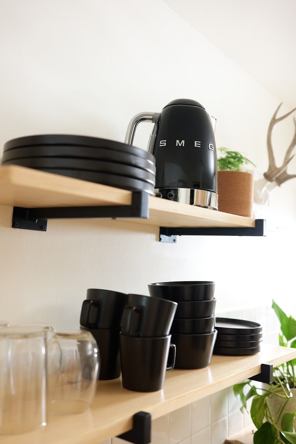 Una repisa en la cocina con tazas de café negro, una cafetera negra y una planta en maceta.
