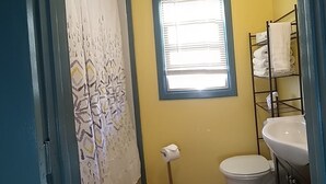 A small bathroom with a toilet, a sink, a window, and a shower curtain. - Sleeping Ute Micro Suite in beautiful SW Colorado (Dolores)