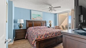 Un dormitorio con una cama de madera, dos mesitas de noche con lámparas, un ventilador de techo y un gran ventanal con vistas al exterior.