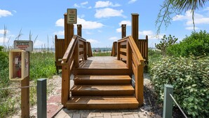 Una escalera de madera que lleva a una zona de playa con carteles que indican los horarios para cocinar a la parrilla y una instalación libre de humo.