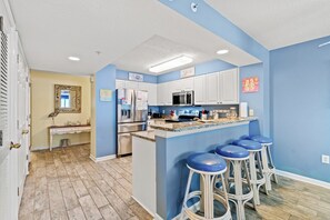 Una cucina con mobili bianchi, un forno a microonde, un frigorifero e un angolo bar con sgabelli.