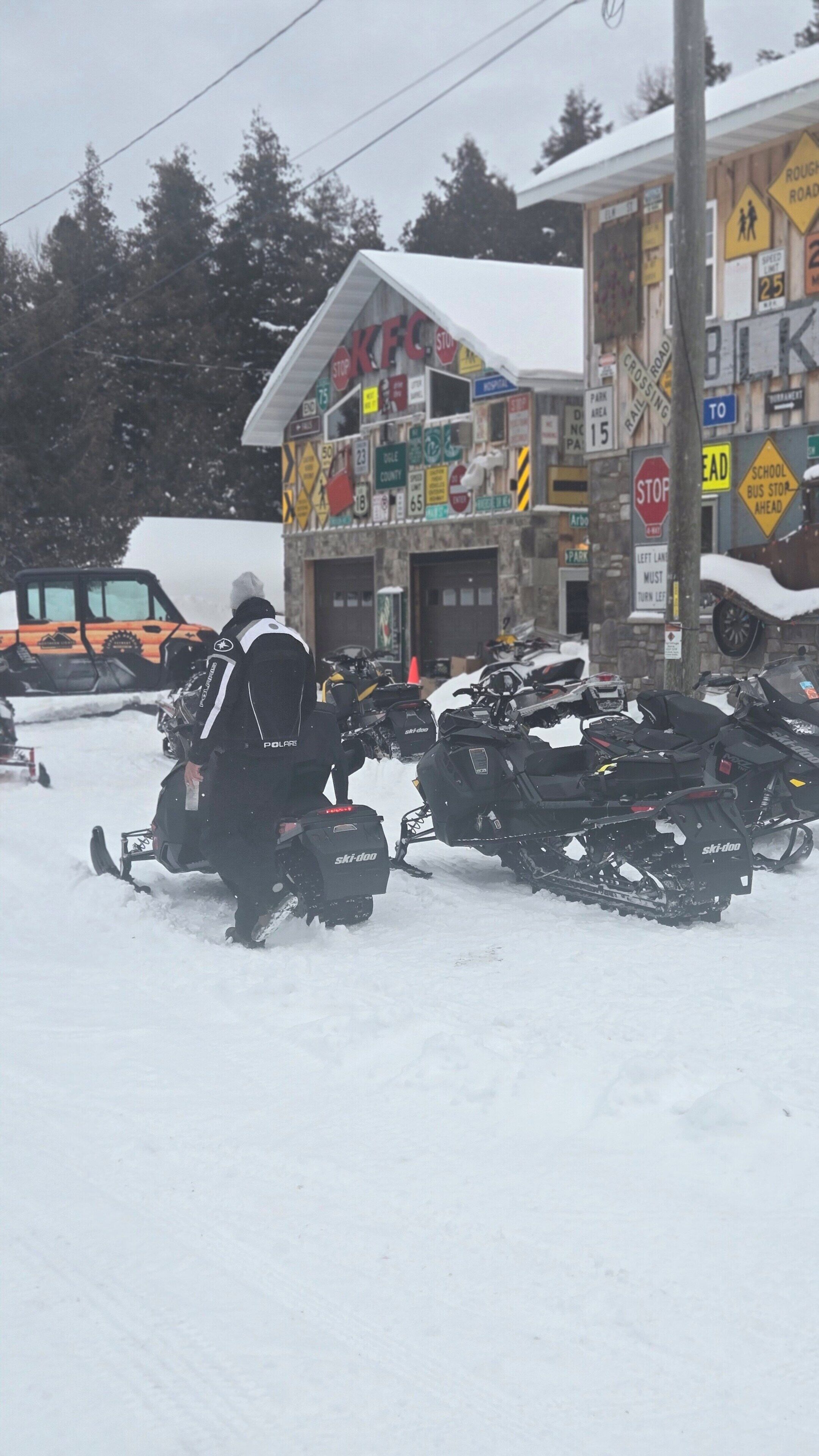 Un edificio con varios carteles y un estacionamiento con motos de nieve.