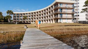 Un hôtel moderne à la façade incurvée, doté de nombreux balcons et d’une promenade en bois menant à un espace verdoyant.