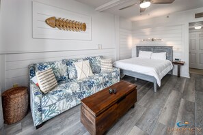 Quarto com cama, sofá, mesa de centro de madeira e escultura de peixe na parede.