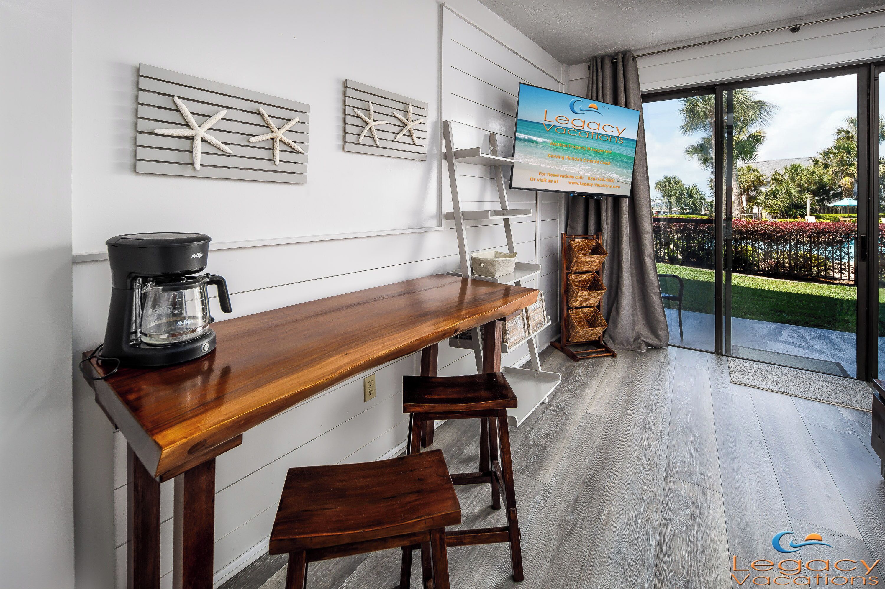 A modern kitchen with a wooden bar counter, a coffee maker, and a view of a pool and palm trees.
