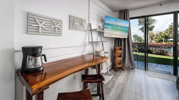 A modern kitchen with a wooden bar counter, a coffee maker, and a view of a pool and palm trees.