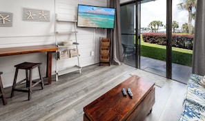 Uma sala de estar moderna com uma mesa de centro de madeira, uma TV fixada na parede, uma varanda com vista para a marina e um espaço de estar com um sofá e poltronas.