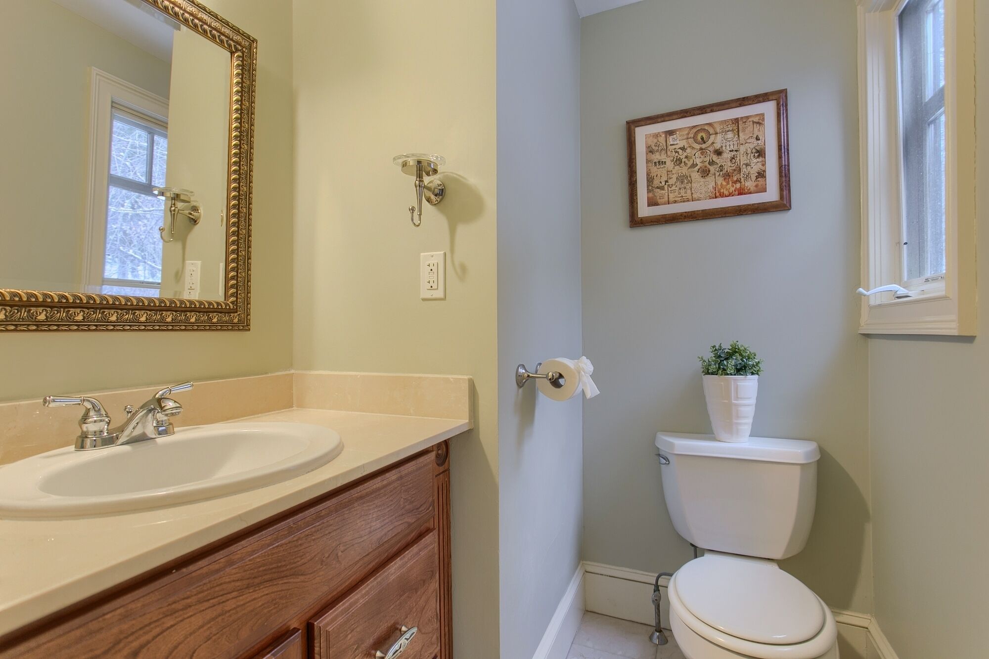 A bathroom with a double sink vanity, a toilet, a framed artwork on the wall, and a window with a view.