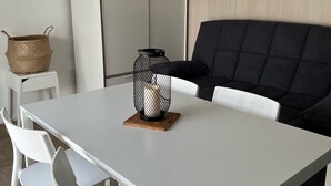 A modern, minimalist living room with a white table, white chairs, a black sofa, and a wooden cabinet. - T2 apartment with garden near the beach (Valras-Plage)