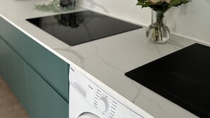 A modern kitchen with a built-in washer and dryer, a black induction cooktop, and a vase with pink roses on the countertop. - T2 apartment with garden near the beach (Valras-Plage)