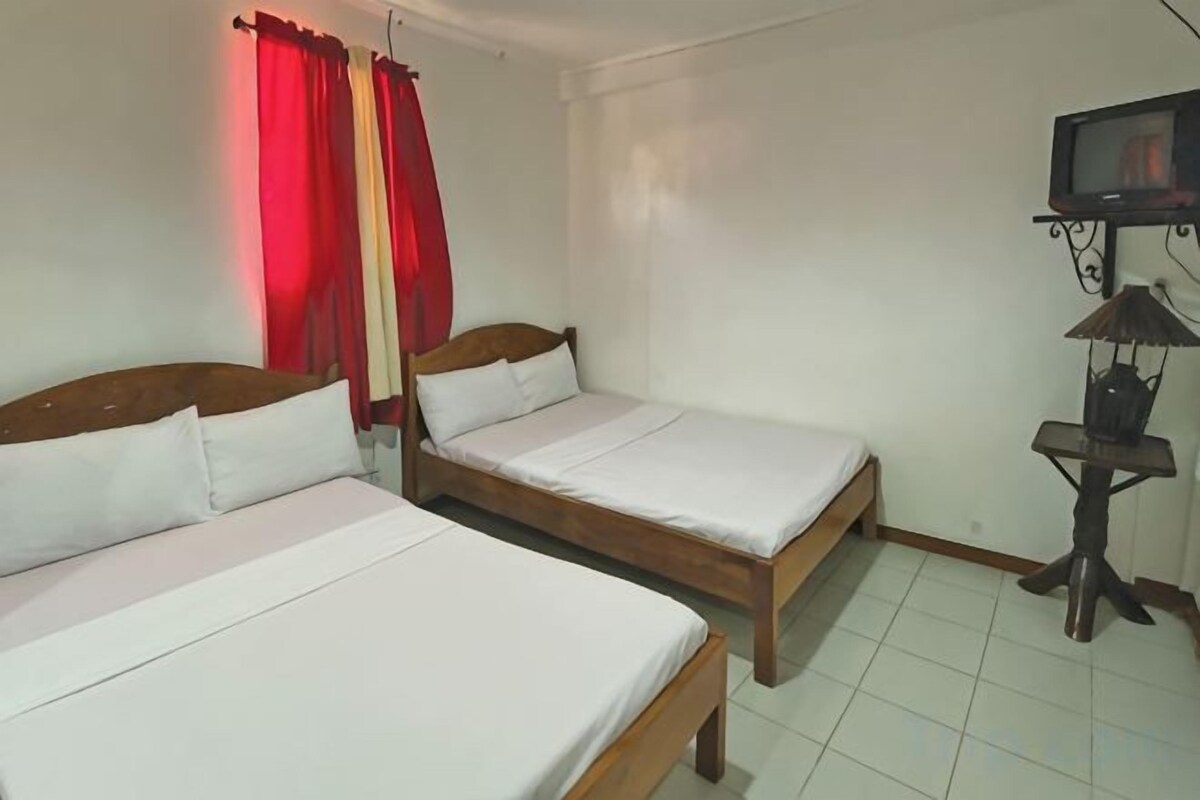 A room with two wooden beds, a television on a stand, and a small table with a lamp.