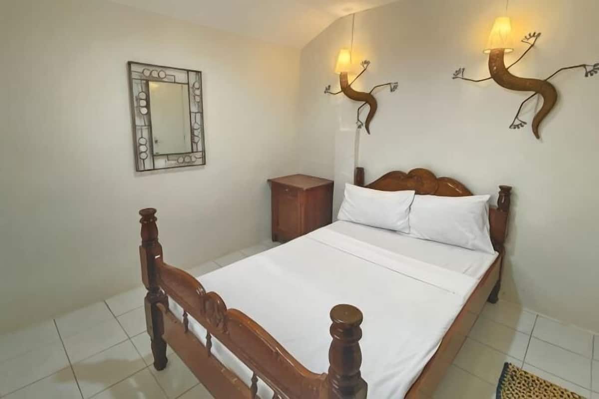 Een slaapkamer met een houten bed, een nachtkastje, een spiegel en wandlampen.
