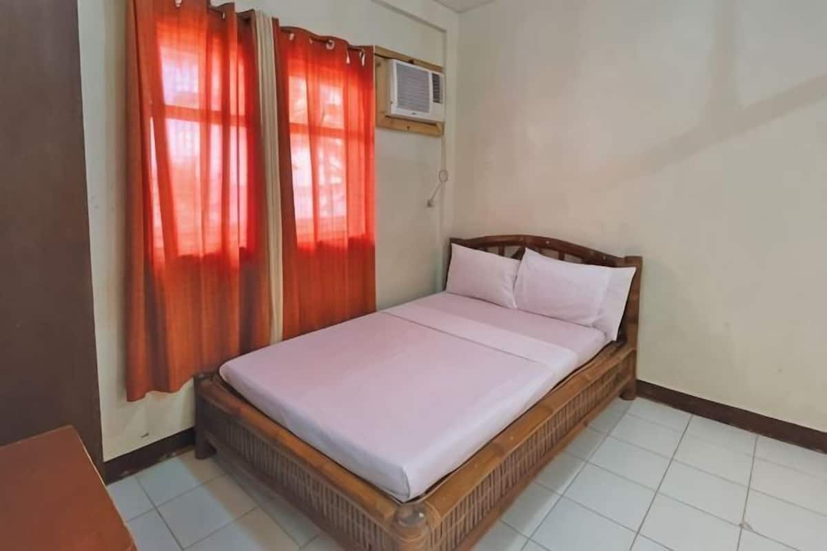 Een eenpersoonsbed met houten frame en witte beddengoed, rode gordijnen en een airconditioning op de muur.