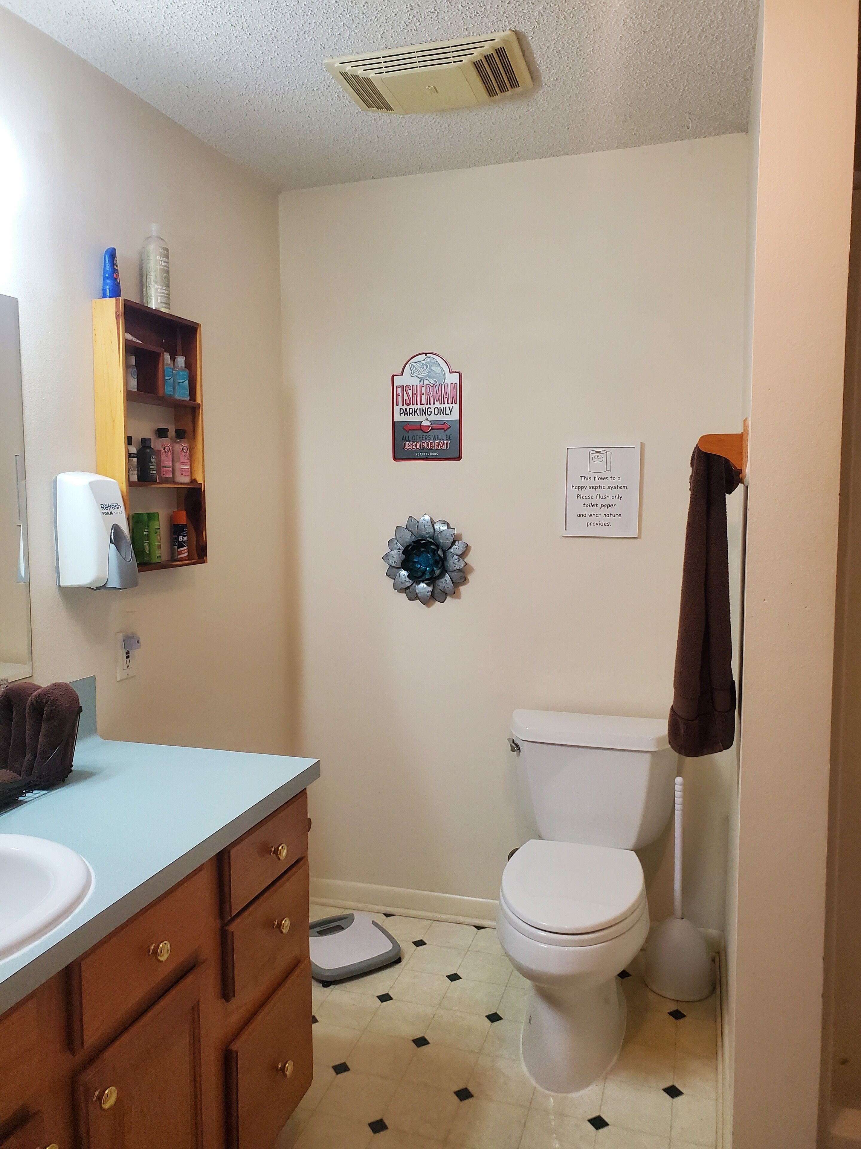 A bathroom with a toilet, a sink, a shower, a towel rack, a soap dispenser, and a sign indicating Fisherman Parking Only.