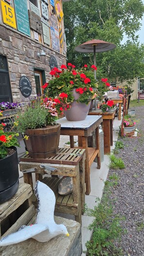 Outdoor seating with potted plants, a stone building with signs, and a wooden table with a white duck decoration.
