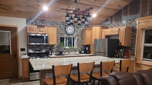 A modern kitchen with wooden cabinets, a large island with bar stools, stainless steel appliances, and a decorative clock. - 3 Bedroom Loft With Game Room ~ In The Heart Of Downtown Copper Harbor (Copper Harbor)
