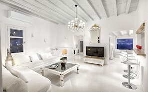 Un salón amplio con un sofá blanco, una mesa de centro de cristal, un televisor y una araña.